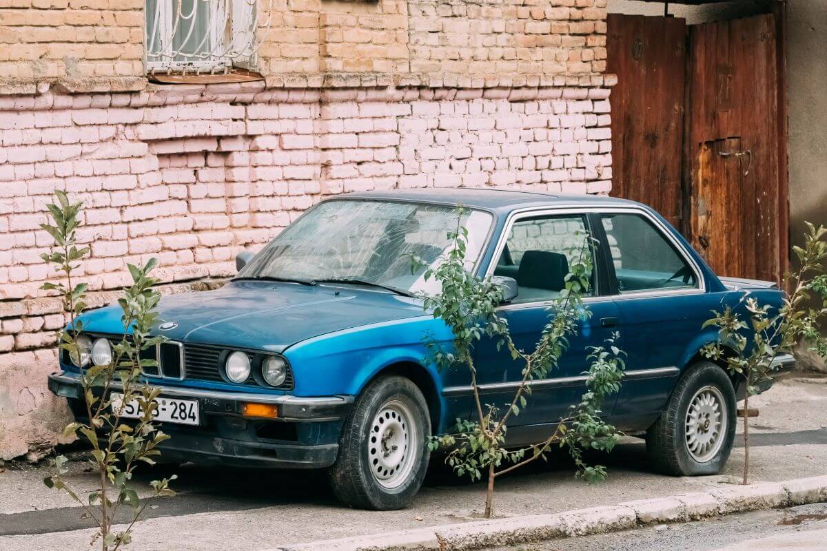 Old blue car parked next to a house