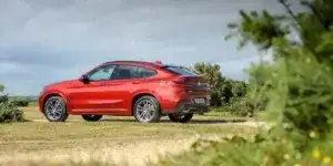 A red BMW X4 SUV parked in a field. The car has a sporty design with large alloy wheels and a sloping roofline.