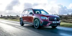 A red Mercedes-AMG GLB 35 SUV driving down a country road with a field of grass in the background.