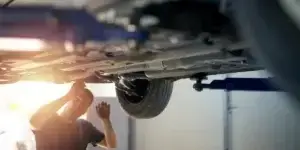 A photo of a mechanic wearing a blue uniform repairing a car. The background is blurred and shows a garage workshop.