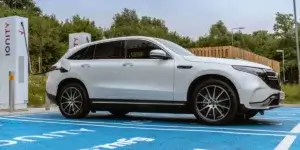 The car in the image is a white Mercedes-Benz EQC. It is an electric SUV that is charging at an electric vehicle charging station. The car has a modern and sleek design, with large wheels and a black grille. The charging station has two charging points, and the car is plugged into one of them.