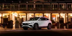 A white Mercedes-Benz EQA electric SUV parked in front of a building with illuminated windows at night.