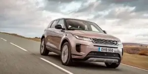 The image shows a Land Rover Range Rover Evoque driving on a winding road surrounded by green hills. The car is a metallic bronze color and has a sleek, modern design. The license plate on the car reads "DV16 SGO."