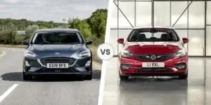 A side-by-side comparison of two cars. On the left is a grey Ford Focus, and on the right is a red Vauxhall Astra. Both cars are parked in different locations. The Ford Focus is on a road with a scenic landscape in the background, while the Vauxhall Astra is parked in a garage-like setting.