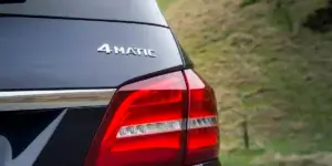 A close-up photo of the rear of a dark gray Mercedes-Benz SUV. The car's taillight is illuminated and the "4MATIC" emblem is prominently displayed.