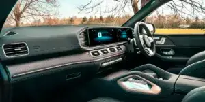 The interior of a Mercedes-Benz GLE SUV. The dashboard features a large touchscreen display, and the seats are upholstered in black leather. The steering wheel has multiple buttons for controls, and the center console includes a gear selector and other buttons.