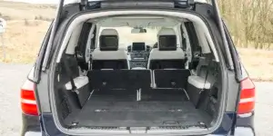 The image shows the cargo area of a Mercedes-Benz GLS. The rear seats are folded down to create a large, flat loading space. The interior looks luxurious with white leather upholstery and a carpeted floor. There is a large storage compartment under the floor.