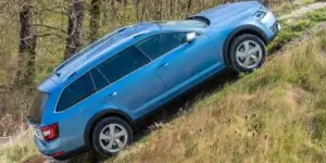 A blue Skoda Octavia Scout estate car driving up a steep hill in a forest. The car has all-terrain tires and is equipped with features for off-road driving.