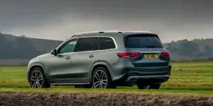 The car in the image is a Mercedes-Benz GLS. It is a large luxury SUV with a sleek and modern design. The car is parked on a grassy field with a cloudy sky in the background.