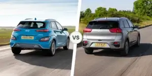 A side-by-side comparison of the Hyundai Kona Electric and Kia e-Niro. The Hyundai Kona Electric is blue and the Kia e-Niro is silver. Both cars are driving on a road with green fields in the background.