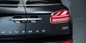 The image shows the rear of a black MINI Clubman. The car has distinctive Union Jack-inspired taillights and the word "CLUBMAN" written across the tailgate. The badge also says "COOPER," indicating the specific model.