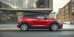 A red Nissan Juke parked on a city street in front of a modern building. The car has a sporty design with black accents and alloy wheels.