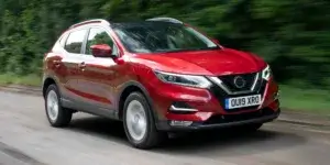 A red Nissan Qashqai driving on a winding road with trees on either side.