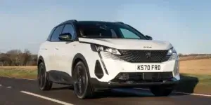 Peugeot 3008 driving on a winding road with trees on either side.