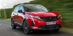 A red Peugeot 3008 driving on a winding road with trees on either side.