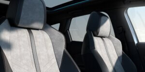 The interior of a car with two front seats upholstered in a combination of gray fabric and leather. The seats have a modern design with contrasting stitching and a large panoramic sunroof above.