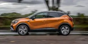 An orange Renault Captur driving down a wet road on a cloudy day. The car is moving fast and is blurred slightly.