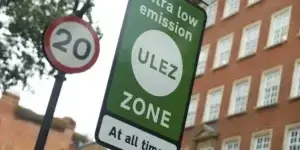 A green sign with the text "Ultra Low Emission Zone" and "ZONE" in white. A circular sign with the number "20" is visible in the background.