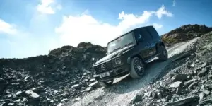 The car in the image is a Mercedes-Benz G-Class. It is a large, rugged SUV that is designed for off-road driving. The car is driving up a steep, rocky hill, and it looks like it is having no trouble. The car has a black exterior and large off-road tires. It also has a roof rack and a spare tire mounted on the back.