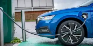 A blue Skoda Octavia iV plug-in hybrid car charging at an electric vehicle charging station. The charging cable is plugged into the front fender of the car.