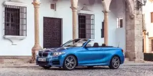 A blue BMW 2 Series Convertible parked in front of a historic building with a stone facade and arched doorways.