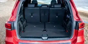 The image shows the cargo area of a red Mercedes-Benz GLB. The rear seats are folded down to create a large, flat loading space. The interior looks spacious and practical, with a carpeted floor and a cargo cover. There is a large storage compartment under the floor.