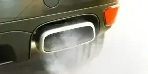 A car exhaust pipe emitting white smoke. The car's rear bumper is partially visible in the background.