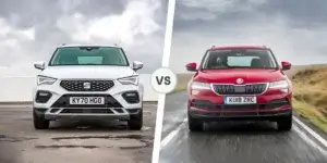 A comparison of a white SEAT Ateca and a red Skoda Karoq. The SEAT Ateca is driving on a road surrounded by trees, and the Skoda Karoq is driving on a road surrounded by hills. The two cars are separated by the word "VS.