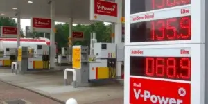 A Shell gas station with V-Power branding displaying fuel prices: unleaded at 159.9, diesel at 135.9, and autogas at 68.9. Several fuel pumps and signage are visible in the background.