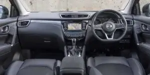 The interior of a Nissan Qashqai. The car has a black dashboard with a large touchscreen display, a leather steering wheel, and black leather seats.