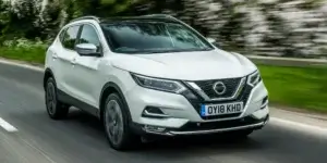 A white Nissan Qashqai driving on a winding road with trees on either side.