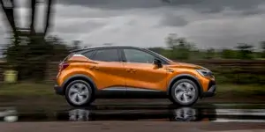 An orange Renault Captur driving down a wet road on a cloudy day. The car is in motion and slightly blurred.