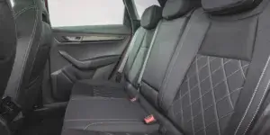 The backseat of a Skoda Karoq SUV. The seats are upholstered in black leather with diamond stitching and are split-folding. The headrests are adjustable and there are door pockets with cup holders.