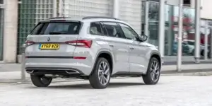 A silver Skoda Kodiaq SUV driving down a city street. The rear of the car is visible, showing the taillights, rear spoiler, and alloy wheels.