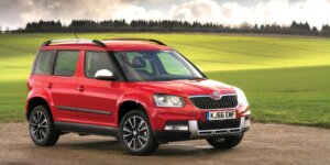 A red Skoda Yeti SUV parked in a field with a green background. The car has a rugged exterior with black accents and roof rails.