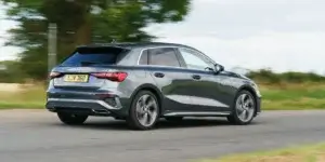 A gray Audi A3 Sportback car driving on a road with trees and a field in the background. The car is in motion, and the rear of the car is visible, showing the taillights, rear bumper, and license plate. The license plate on the car is LJV 360.