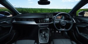 The interior of an Audi A3 Sportback car. The dashboard features a large touchscreen display, and the seats are upholstered in black leather. The steering wheel has multiple buttons for controls, and the center console includes a gear selector and other buttons.