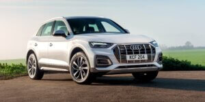 A white 2021 Audi Q5 SUV parked on a road with a field in the background. The car has a sleek and modern design with large alloy wheels and a prominent grille. The license plate on the car is KCF 204.