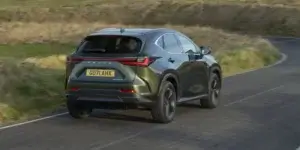 A green Lexus UX 250h SUV driving on a winding road with a scenic landscape in the background. The car is in motion, and the rear of the car is visible, showing the taillights, rear bumper, and license plate. The license plate on the car is GU71 AHX.