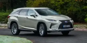 A beige Lexus RX 450h SUV driving on a road with trees in the background. The car has alloy wheels and a modern design. The license plate on the car is GX69 YJH.