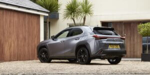 A gray Lexus UX 250h SUV parked in a driveway in front of a modern house. The car has black alloy wheels and a sleek design. The license plate on the car is GU21 CVD.