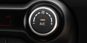 A close-up of an air conditioning control knob in a car. The knob is black with a silver ring, and it features a fan icon, temperature lines, and A/C labels. The current temperature setting is highlighted in orange.