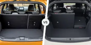 A side-by-side comparison of the trunks of two cars. On the left is the trunk of a yellow Ford Fiesta, with the rear seats folded down to reveal a spacious cargo area. On the right is the trunk of a white Vauxhall Corsa, also with the rear seats folded down, but with a slightly smaller cargo area.