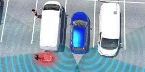 An aerial view of a blue car parked in a parking lot between two white vans. The blue car's rear parking sensors are activated, as indicated by the blue lines extending outwards from the car. A person is walking behind the white van on the right side of the image.