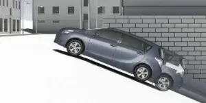 A gray Toyota Verso car parked on a steep hill with a wall behind it. The car's wheels are turned to prevent it from rolling backwards. The arrow indicates the direction of the steering wheel.