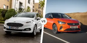 A side-by-side comparison of two cars. On the left is a white Ford Fiesta parked on a street in front of a building. The license plate on the car is AE67 ZHP. On the right is an orange Vauxhall Corsa driving on a road with a scenic landscape in the background. The license plate on the car is BN69 CWD.