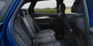 The rear seats of a blue Audi Q5 or Q5 Sportback. The seats are upholstered in black leather with a diamond pattern and have headrests. The windows show a scenic countryside landscape.