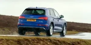 A blue Audi Q5 driving on a wet road in the countryside. The car is facing away from the viewer and has a license plate that reads "KY23 PNZ."