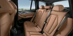 The rear seats of a BMW X3. The seats are upholstered in beige leather and have headrests. The windows show a scenic countryside landscape.