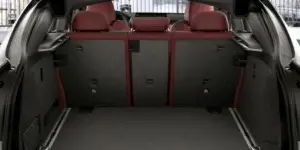 The trunk of a BMW X4 with the rear seats folded down. The trunk is carpeted and features a flat floor. The rear seats are upholstered in red leather and have headrests. There is a small amount of luggage visible in the trunk.